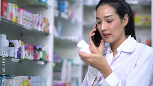 Pharmacists woman talking on a mobile phone while holding a pill bottle ordering a prescription from a pharmacy