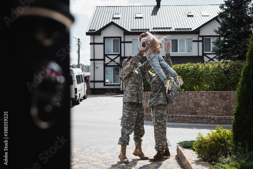 Father and mother in military uniforms lifting daughter in air, while standing on street on blurred foreground