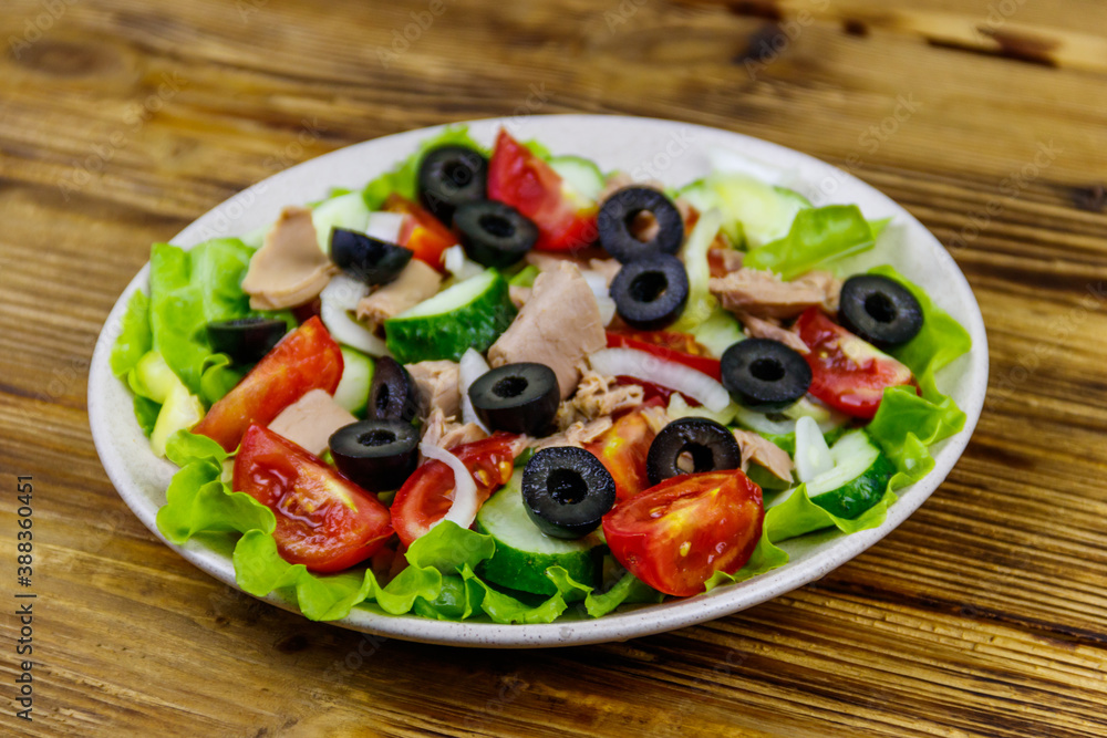 Tasty tuna salad with lettuce, black olives and fresh vegetables on wooden table