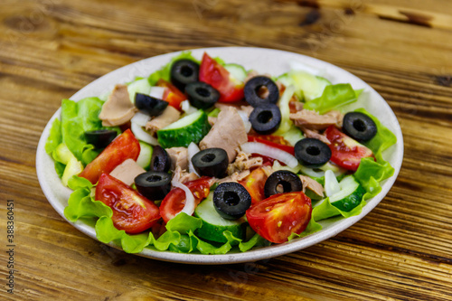 Tasty tuna salad with lettuce, black olives and fresh vegetables on wooden table