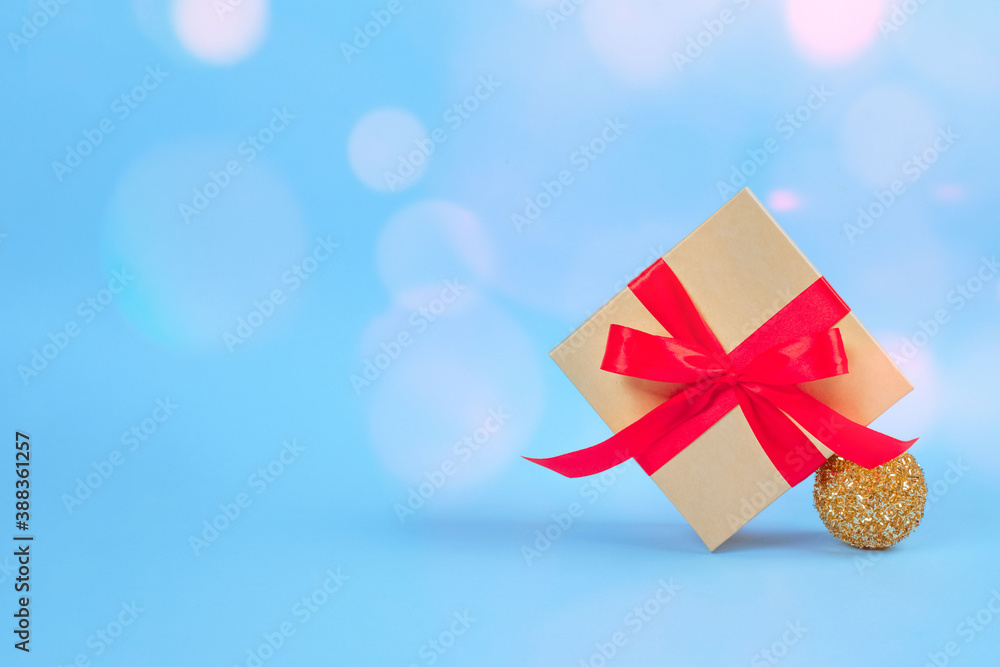 Present box with red bow and Christmas tree decorations on festive blue background with blurred bokeh and copyspace for your text. Christmas and New Year celebration concept Present box with red bow and Christmas tree decorations on festive blue background with blurred bokeh and copyspace for your text. Christmas and New Year celebration concept