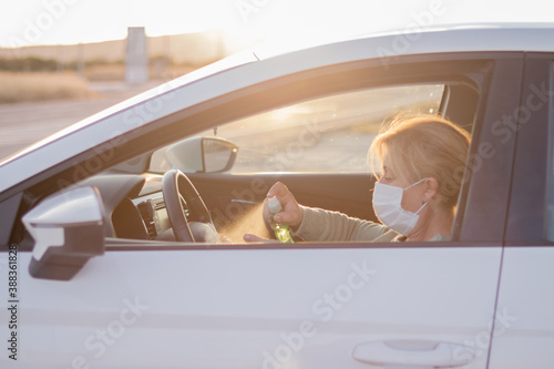 Mujer con mascarilla en su vehículo desinfectándose las manos