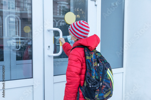 schoolboy in medical face mask is near door and pulls handle before entering school. New reality, restrictions to prevent covid pandemic. Healthcare concept photo