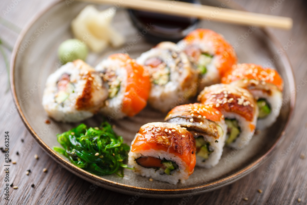 Sushi maki rolls with salmon, eel, avocado, cucumber on a plate with chopsticks, soy sauce, wasabi and ginger. Japanese traditional fish food closeup served for lunch in modern gourmet restaurant Sushi maki rolls with salmon, eel, avocado, cucumber on a plate with chopsticks, soy sauce, wasabi and ginger. Japanese traditional fish food closeup served for lunch in modern gourmet restaurant