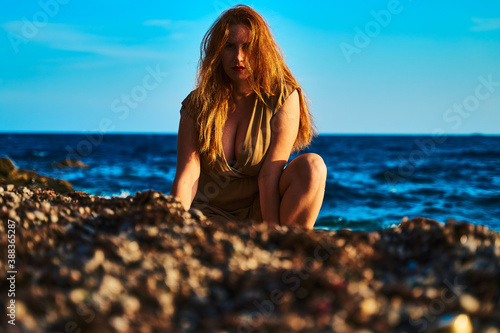 Portrait of a girl with red hair developing in the wind with an open neckline against the background of the sea
