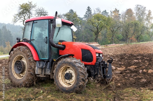 Red tractor on a muddy field. Agricultural work. Autumn foggy morning on the farm. Agriculture machinery. © martinfredy