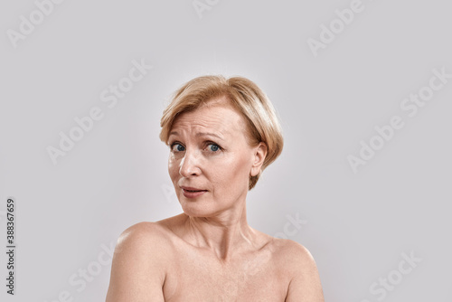 Close up portrait of attractive middle aged woman looking at camera while posing  standing against grey background. Human facial expressions  emotions  reaction concept
