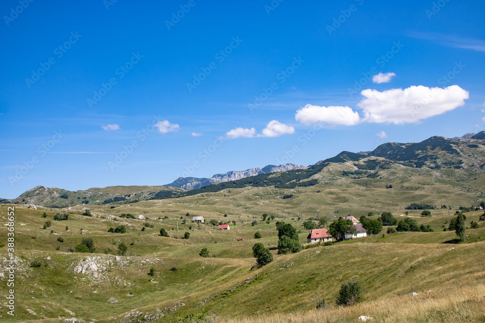 Fantastic mountain views in Montenegro. The hills are covered with grass and trees. Beautiful blue sky. Village in the hills.