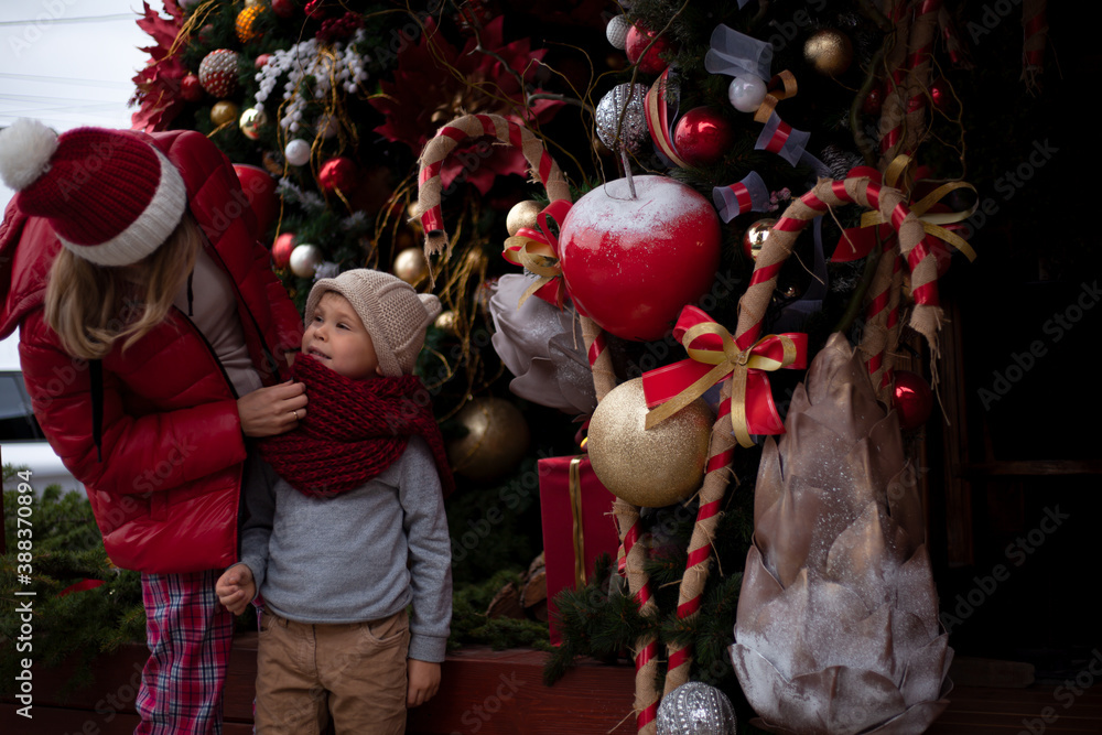 Obraz premium Happy family, young pretty woman with child spend time together outdoor at the background decorated christmas tree with lights garland on New Year's Eve holidays.