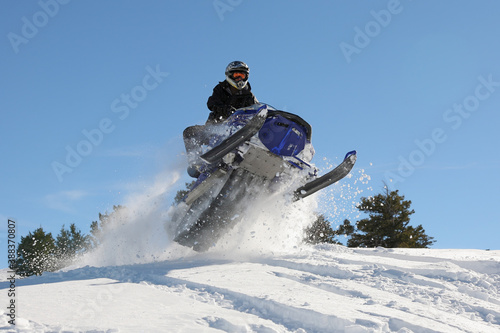 extreme snowmobile rider jumping machine through powder in mountains