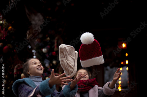Two pretty pteteen girls holds the gift outdoor at the background decorated christmas tree with lights garland on New Year's Eve holidays. Kid dressed warm jacket, red knitted scarf , hat