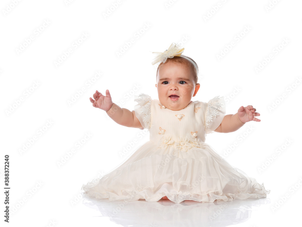 beautiful baby child in a festive dress and a headband, sitting on the floor and joyfully raised her hands. shot on a white background. beautiful baby child in a festive dress and a headband, sitting on the floor and joyfully raised her hands. shot on a white background.