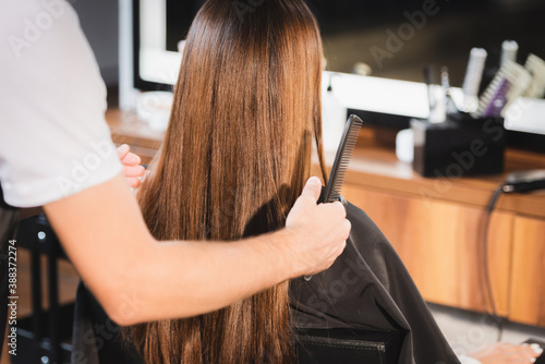 hairstylist holding comb and touching hair of woman on blurred foreground