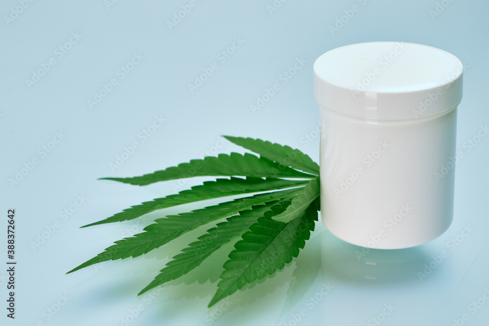 Leaf of cannabis and plastic package or jar with copy space with cream contained hemp oil Leaf of cannabis and plastic package or jar with copy space with cream contained hemp oil
