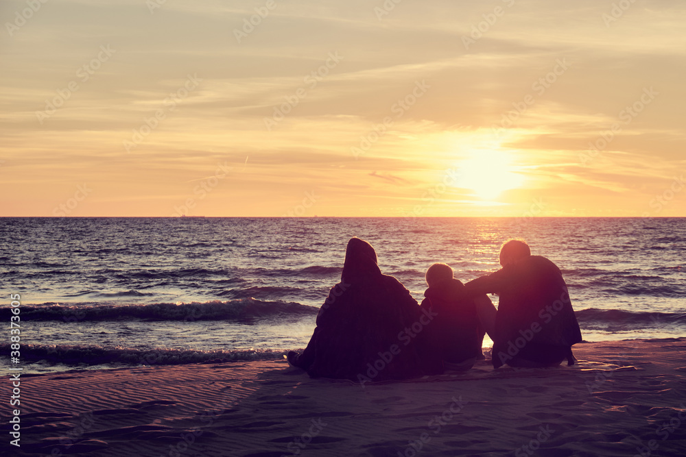 Three people sitting on the beach at sunset