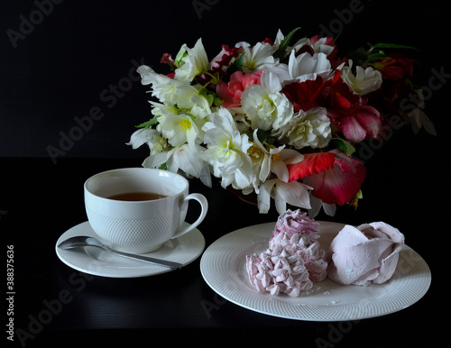 Marshmallows on a white plate next to a Cup of tea.