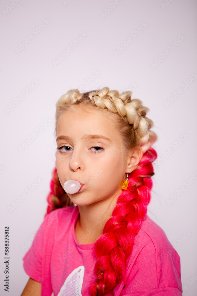 a cute girl in bright multicolored clothes and with colored braids blows bubbles from gum a cute girl in bright multicolored clothes and with colored braids blows bubbles from gum