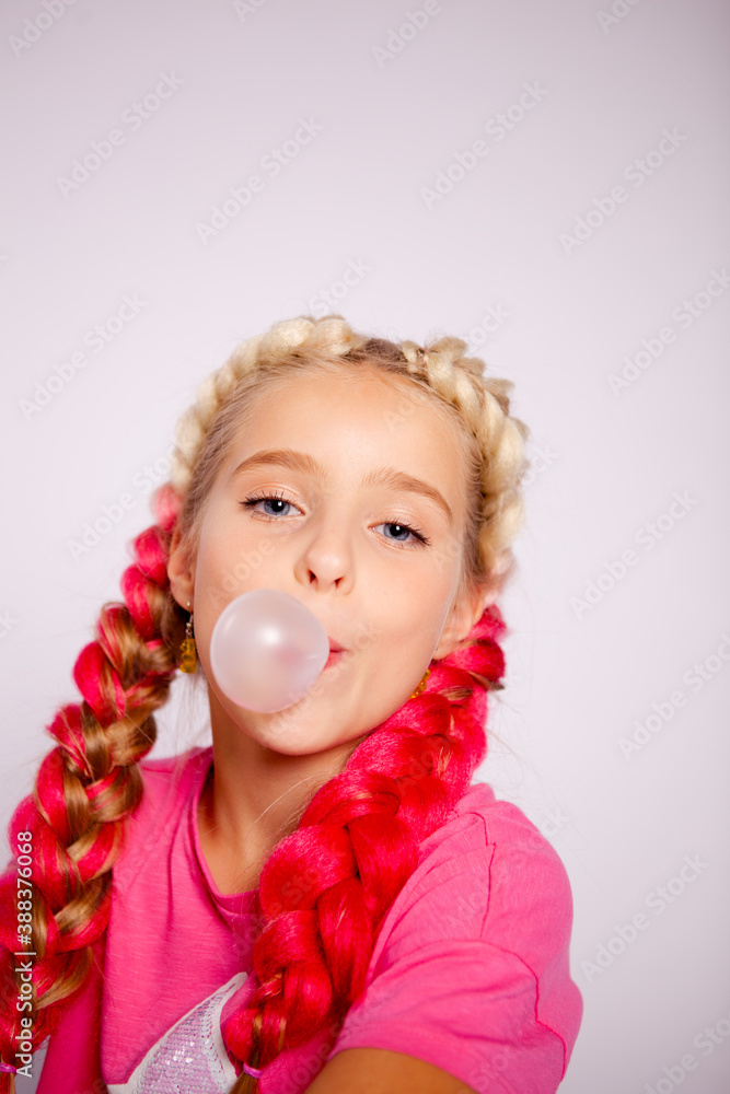 a cute girl in bright multicolored clothes and with colored braids blows bubbles from gum a cute girl in bright multicolored clothes and with colored braids blows bubbles from gum