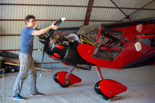 Repairman turning the propeller of small red aircraft in hangar. Small aviation.