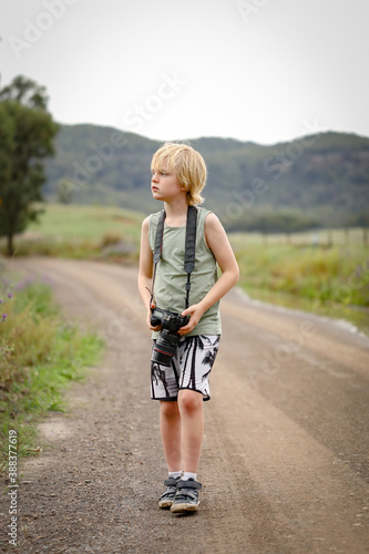 Little boy outdoors in pretty country location taking photos with dslr full frame camera. Vertical orientation