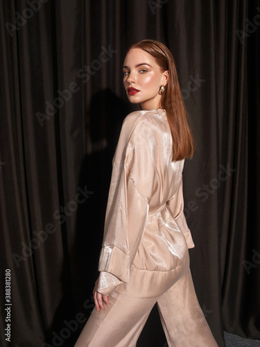 Elegant caucasian woman in beige kimono costume posing against black curtains. Fashion portrait. Elegant stylish caucasian female model with perfect makeip and hairstyle