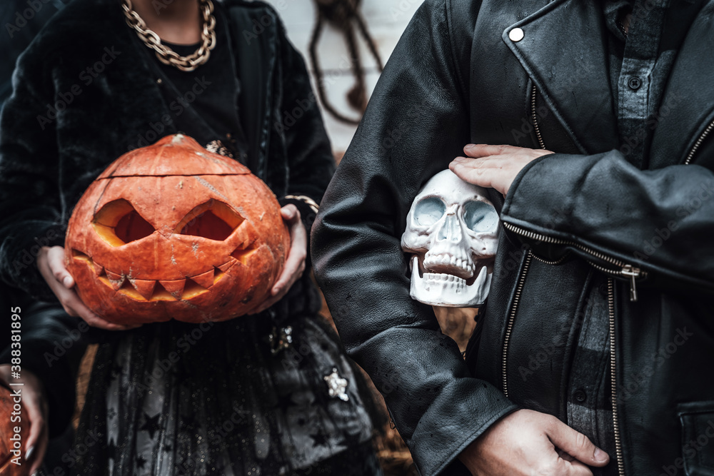 Pumpkins jack-o-lantern and skull in hands. Scary family father,daughter celebrating halloween. Stylish witch costumes, images. Horror,fun at children's party. Hay on street near barn. Black jackets