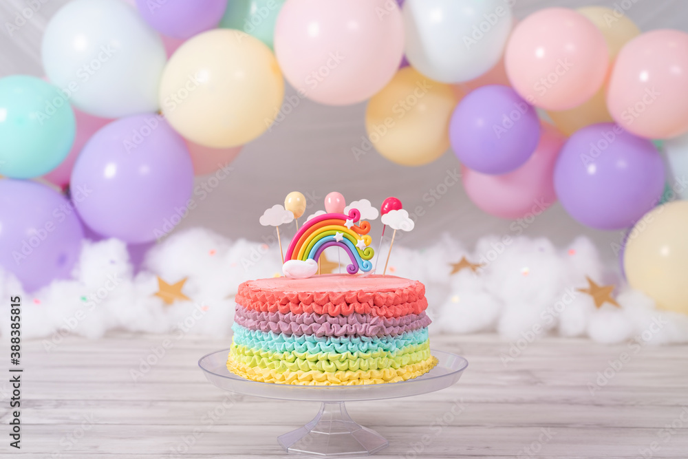 Colorful birthday cake. Rainbow cake with pastel colored balloons. Fantasy birthday. Celebration. Smash the cake photoshoot. Vertical photo.