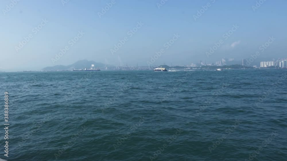 Large distant contemporary passenger ship sails along azure sea water with waves against huge mountain silhouette and city under clear blue sky, on nice sunny day
