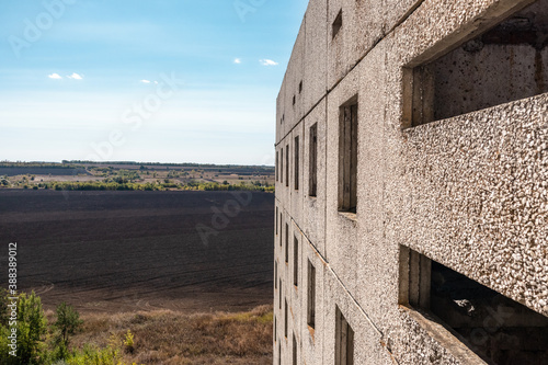 View from window of high multistorey abandoned soviet building with facade on bright blue rural landscape. Weathered housing estate, unfinished city of nuclear scientists in Birky, Ukraine photo