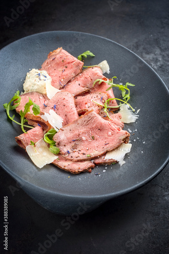 Modern style traditional lunch meat with sliced cold cuts roast beef with rocket salad and parmesan cheese offered as close-up in a modern design plate