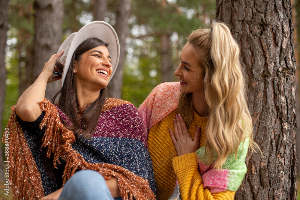 Fototapeta premium Two beautiful women are sitting, talking and smiling in the forest-park