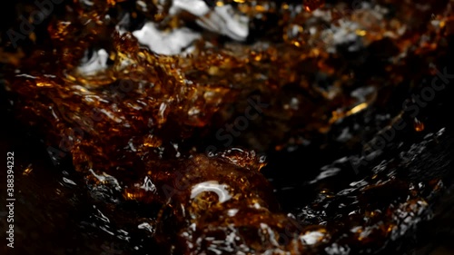 Dark sparkling liquid pouring splashing in slow motion on black background, drinks concept. Dark soda, dark beer, kvass, lager, black Ipa, brown Ale, Stout, Porter, Dunkel, Bock, Dunkelweizen