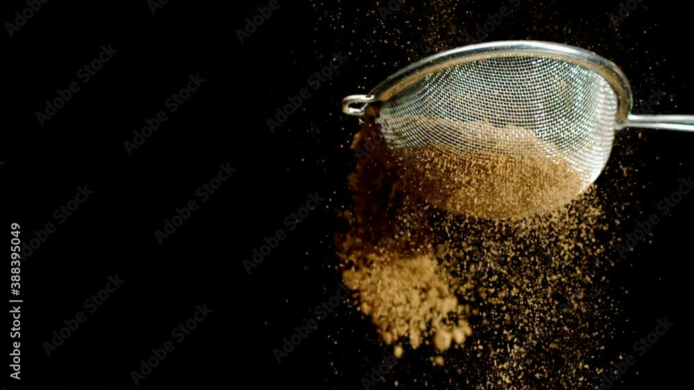 Sprinkling light brown powder in strainer. Beige airy cinnamon cocoa powder sifting with sieve in slow motion isolated on black background. Cooking, baking, decorating garnishing dessert, concept Sprinkling light brown powder in strainer. Beige airy cinnamon cocoa powder sifting with sieve in slow motion isolated on black background. Cooking, baking, decorating garnishing dessert, concept