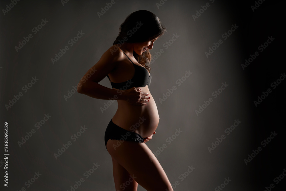 Young pregnant ballerina posing in black underwear in studio - obrazy, fototapety, plakaty 