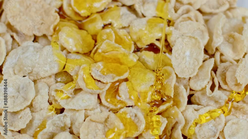 Close-up floral honey covering corn flakes with milk in slow motion, sweet golden fruity caramel sauce dripping. Organic food concept. Nutrition, morning breakfast cereal, clean eating, natural sugars Close-up floral honey covering corn flakes with milk in slow motion, sweet golden fruity caramel sauce dripping. Organic food concept. Nutrition, morning breakfast cereal, clean eating, natural sugars
