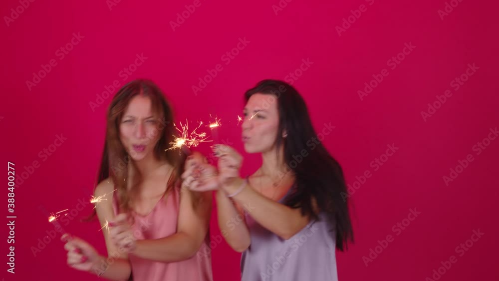 lesbian couple of two pretty young girls dancing with Burning sparklers on red studio background having fun celebrating Christmas and New Year. Female Same Sex Couple in festive mood lesbian couple of two pretty young girls dancing with Burning sparklers on red studio background having fun celebrating Christmas and New Year. Female Same Sex Couple in festive mood