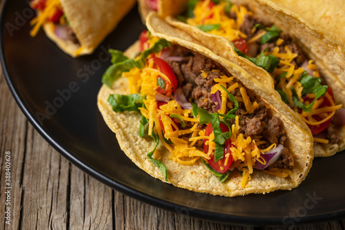 Close-up view of tasty mexican tacos with meat on black round plate on rustic wooden table. Traditional mexican cuisine.
