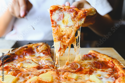 Картината върху платно Wood fire cheesy pizza slice in hand