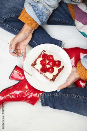 Modelo femenina en botas rojas y denim sosteniendo torta red velvet crema de queso bizcocho de limón rojo topping de frutillas plano cenital vista aérea sobre plato de cerámica blanca fondo blanco photo