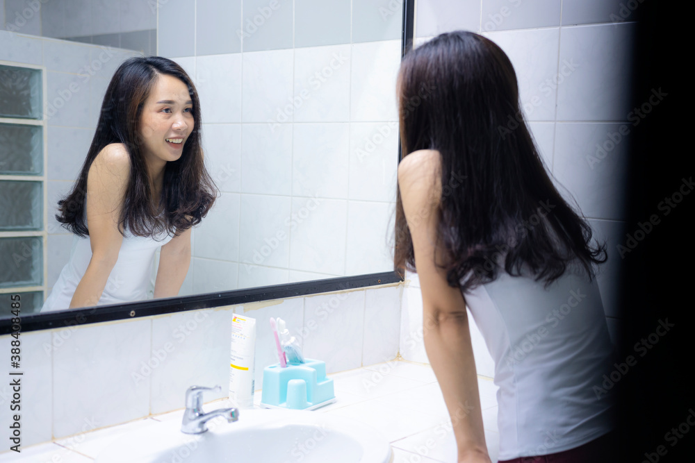 An Asian woman smiling to herself in front of a mirror in the bathroom, a bright new morning. An Asian woman smiling to herself in front of a mirror in the bathroom, a bright new morning.