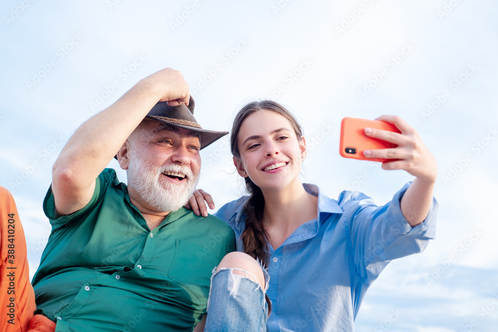 Old man and beautiful young girl are hugging and making selfie. Granddaughter with elderly kind grandfather. Relatives people taking photo or record video. Daughter with mature father. Old man and beautiful young girl are hugging and making selfie. Granddaughter with elderly kind grandfather. Relatives people taking photo or record video. Daughter with mature father.