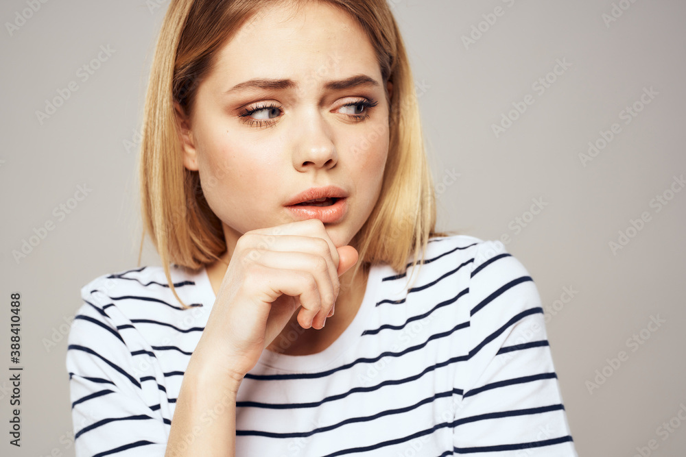 A woman in a striped T-shirt holds her hands in front of her emotions displeasure light background A woman in a striped T-shirt holds her hands in front of her emotions displeasure light background