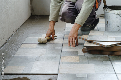 Close up on hands of unknown senior man craftsman using hammer to adjust and lay ceramic tiles on the balcony or terrace over adhesive cement in day - construction industry concept copy space