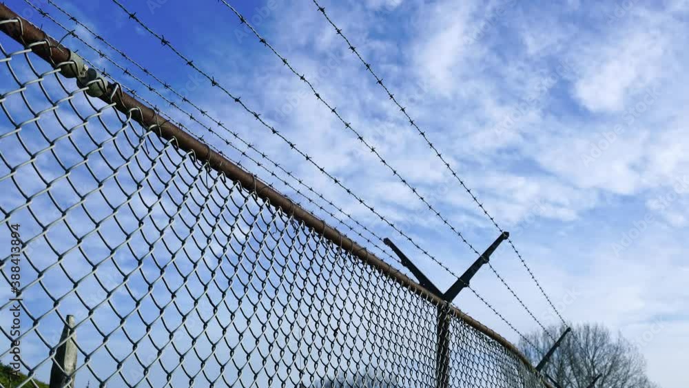 Chain-link fence with barbed wire, floating clouds in blue sky, time-lapse Chain-link fence with barbed wire, floating clouds in blue sky, time-lapse
