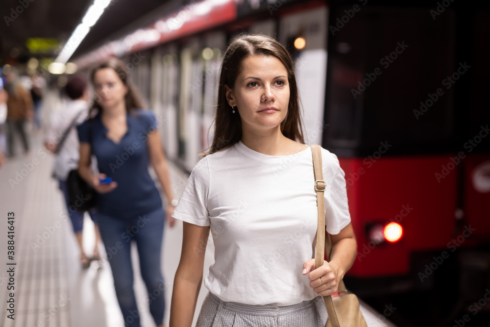 Young woman waiting for subway train, walking at modern underground station..