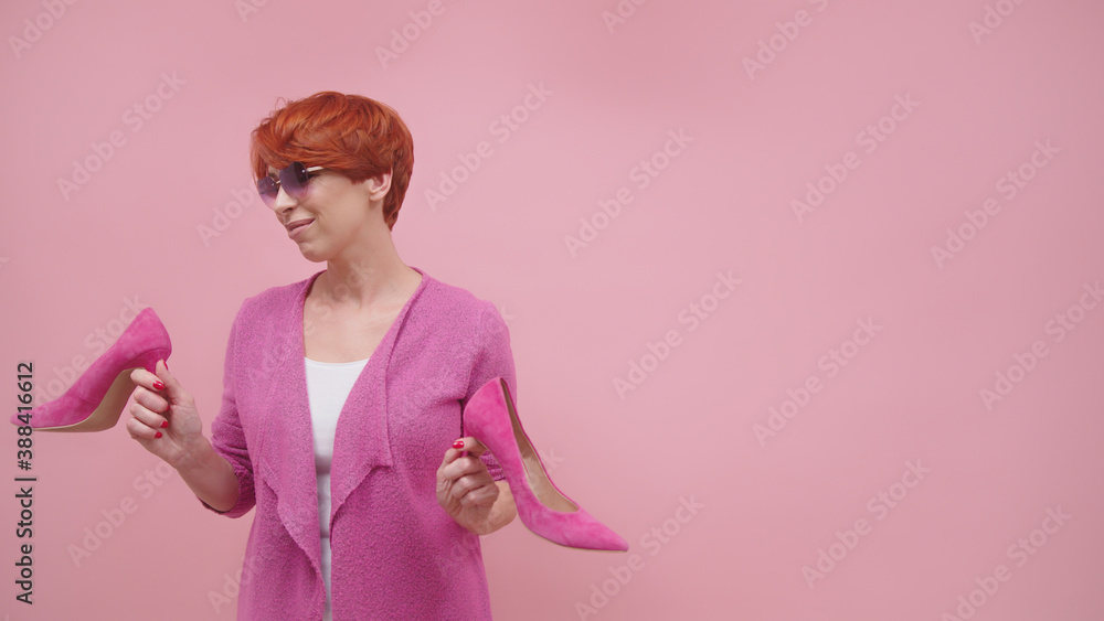 Mature woman with red short hair holding high heal shoes Isolated on purple background. High quality photo Mature woman with red short hair holding high heal shoes Isolated on purple background. High quality photo