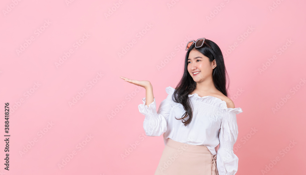 Young smiling Asian woman stand with open palms and looking to copy space on pink background. Young smiling Asian woman stand with open palms and looking to copy space on pink background.