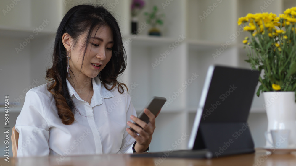 Female using smartphone to relax while working with digital tablet in office room Female using smartphone to relax while working with digital tablet in office room