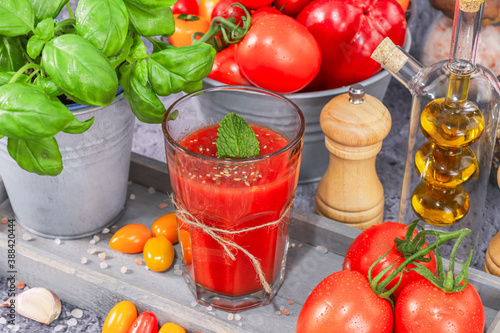 omato juice in a glass
Tomato juice in a glass with basil in a metal bucket, tomatoes, olive oil and spices in a gray tray placed diagonally against a stone background, close-up side view. photo