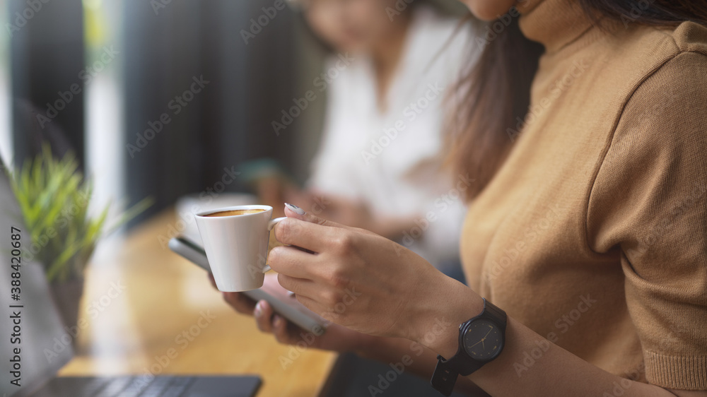 Cropped shot of female using smartphone while holding a cup of coffee Cropped shot of female using smartphone while holding a cup of coffee